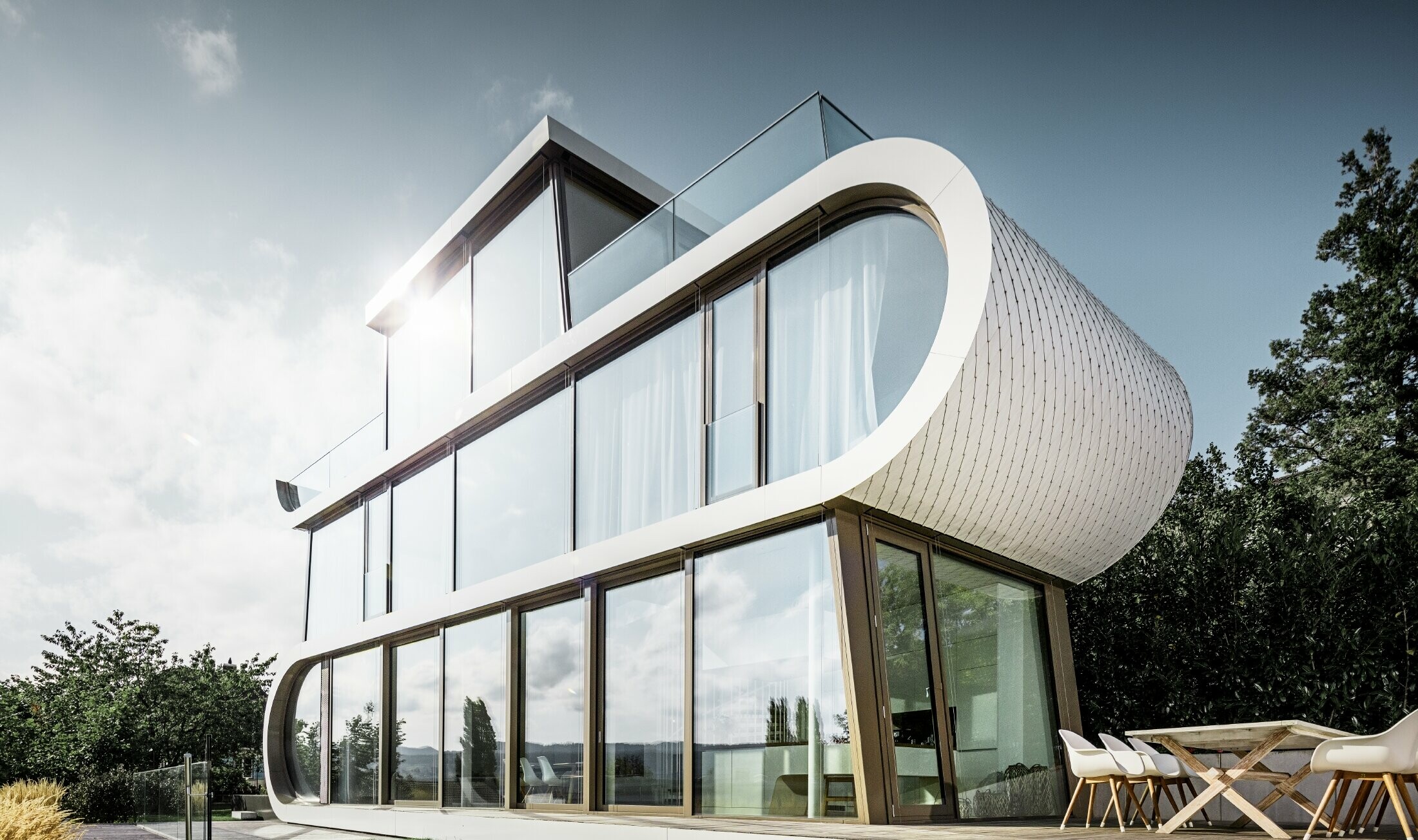 Maison individuelle moderne conçue par l’architecte Stefan Camenzind ; une bande ondulée relie les étages, sur le côté extérieur l’arrondi est recouvert avec les losanges de toiture PREFA faciles à travailler, en petit format, couleur blanc pur.