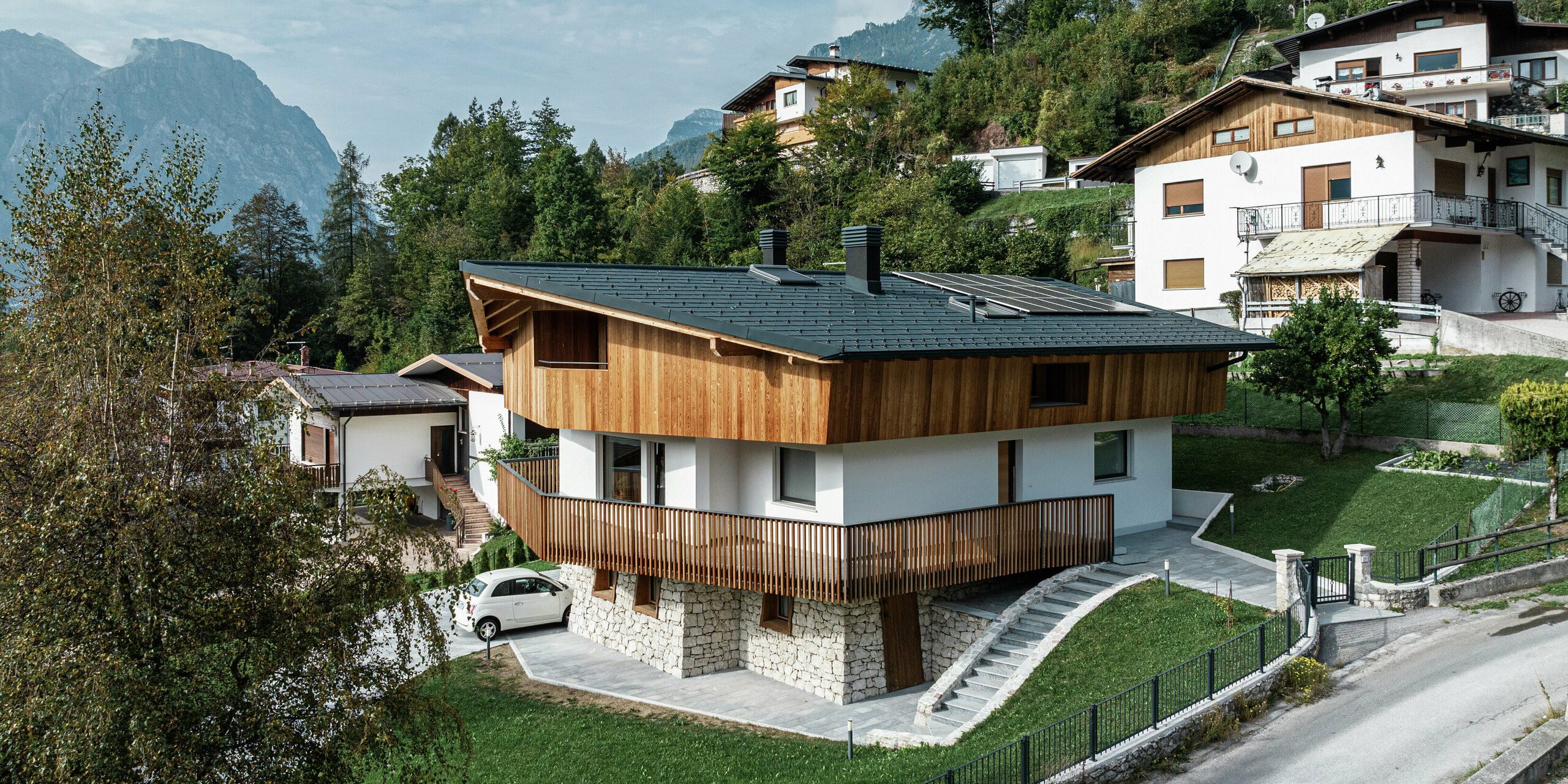 Projet de rénovation à Agordo, Italie : Une maison familiale a été refaite avec une toiture en aluminium PREFA durable en P.10 anthracite. Le PREFA R.16 offre une protection fiable contre les conditions météorologiques extrêmes et garantit une apparence élégante. Le système de gouttière PREFA avec gouttière et tuyau de descente assure également un drainage efficace de l'eau. La combinaison d'une façade en bois naturel, d'une façade en plâtre blanc et d'un toit en aluminium robuste s'intègre harmonieusement dans l'environnement alpin.