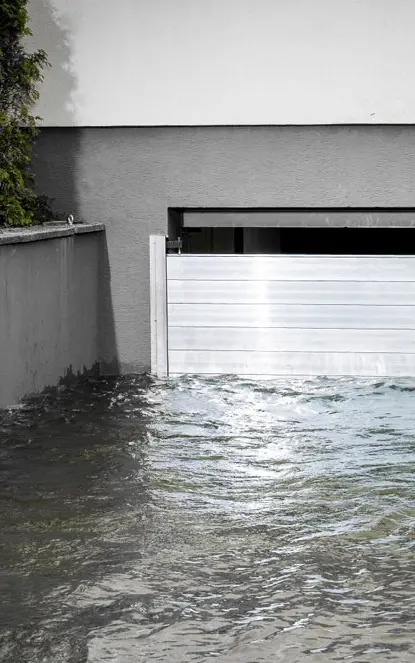 Garageneinfahrt in den Keller mit einem Garagentor das geschützt wird durch den PREFA Hochwasserschutz. Die Einfahrt ist voller Wasser.