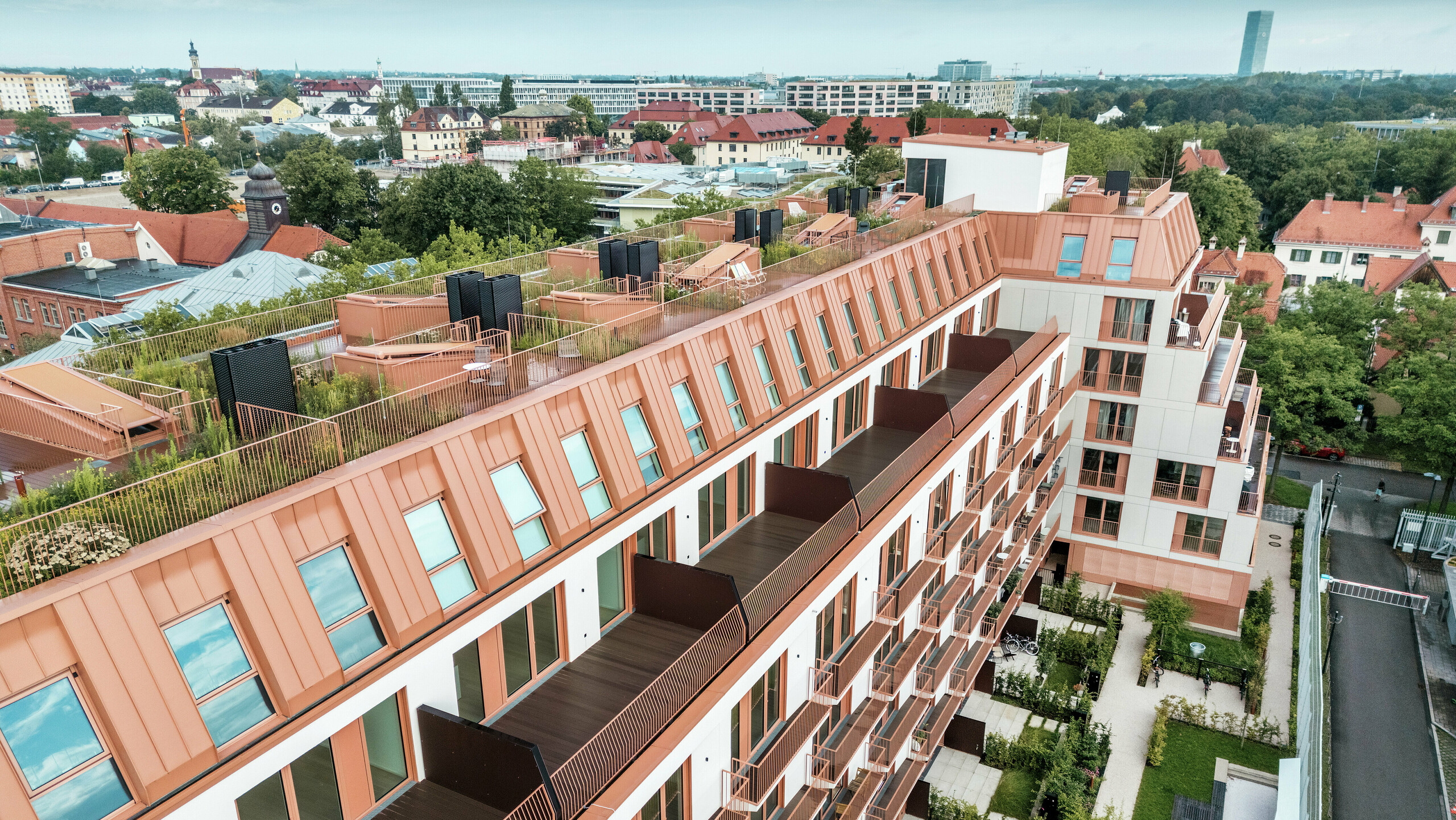 Vue aérienne du projet résidentiel Van B à Munich avec le toit en aluminium PREFALZ remarquable dans la couleur spéciale IGP Orange HDP de PREFA. Des balcons spacieux, des terrasses végétalisées et une conception de façade précise soulignent le concept architectural bien pensé. Idéal pour un développement urbain durable et une vie urbaine avec une qualité de vie et des normes esthétiques élevées.
