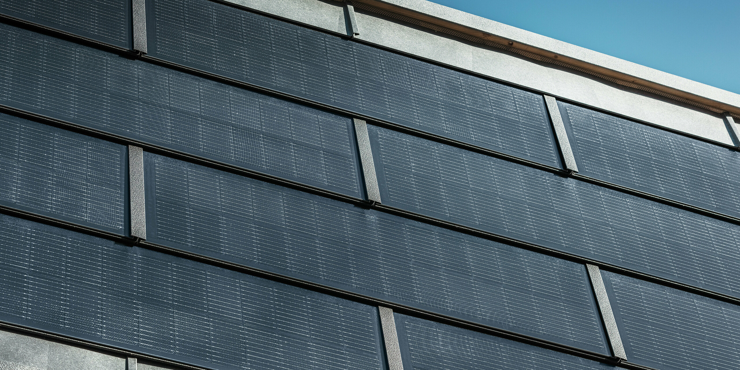 Gros plan sur les tuiles solaires PREFA avec modules photovoltaïques intégrés sur la façade de l'entreprise de couverture RÜMA dans le Vorarlberg, qui combinent design moderne et production d'énergie durable.