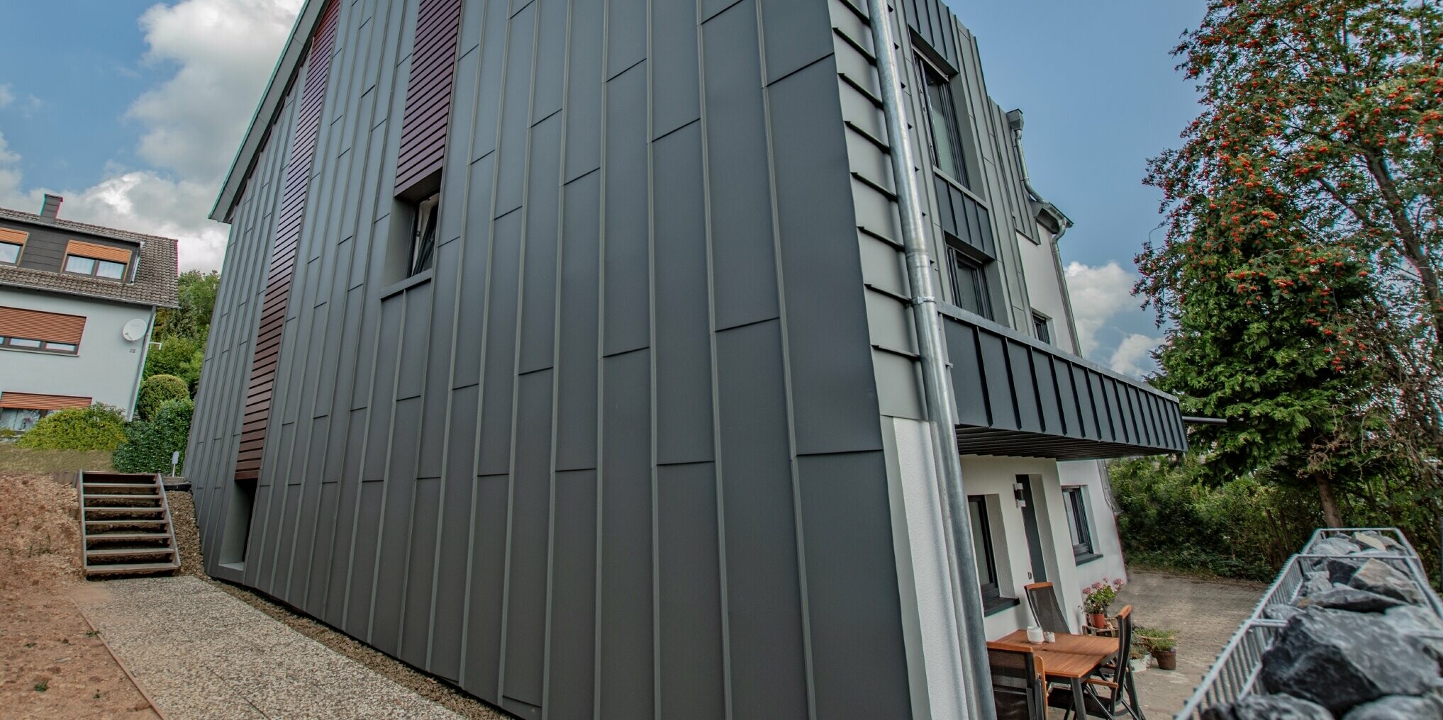 Conception de façade avec façade à agrafage angulaire vertical en gris souris et panneaux de façade posés à l’horizontale, couleur bois foncé. Toute la façade a été réalisée en aluminium par PREFA.