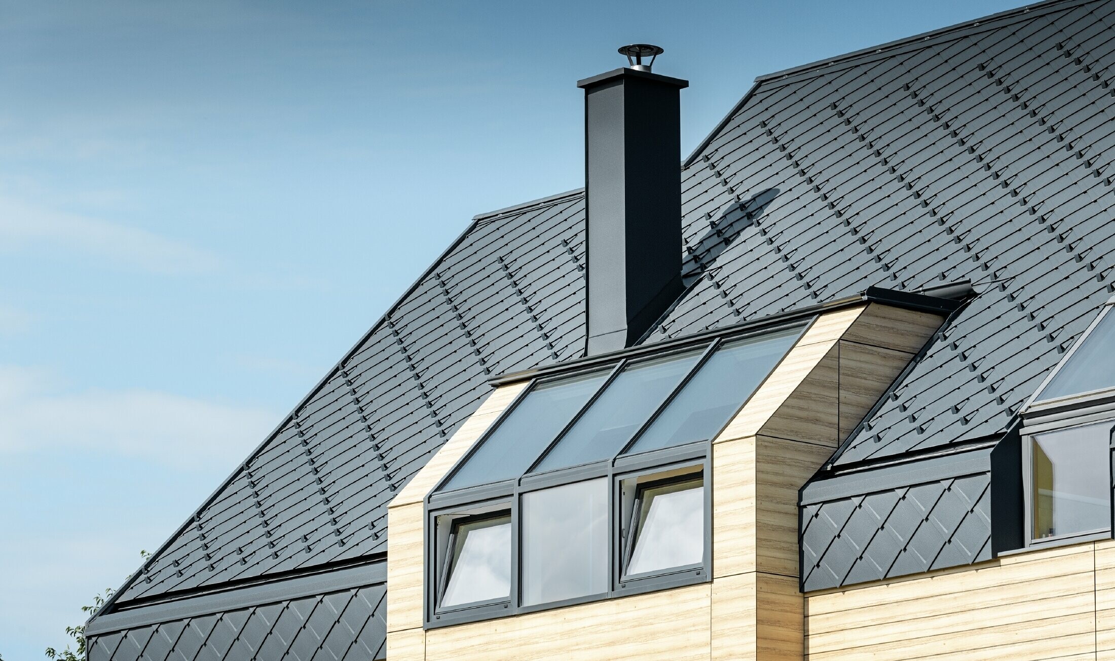 Maison individuelle au toit à deux versants sans saillie de toit — Façade à l’aspect du bois et toiture en aluminium PREFA de couleur anthracite