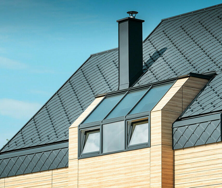Maison individuelle au toit à deux versants sans saillie de toit — Façade à l’aspect du bois et toiture en aluminium PREFA de couleur anthracite
