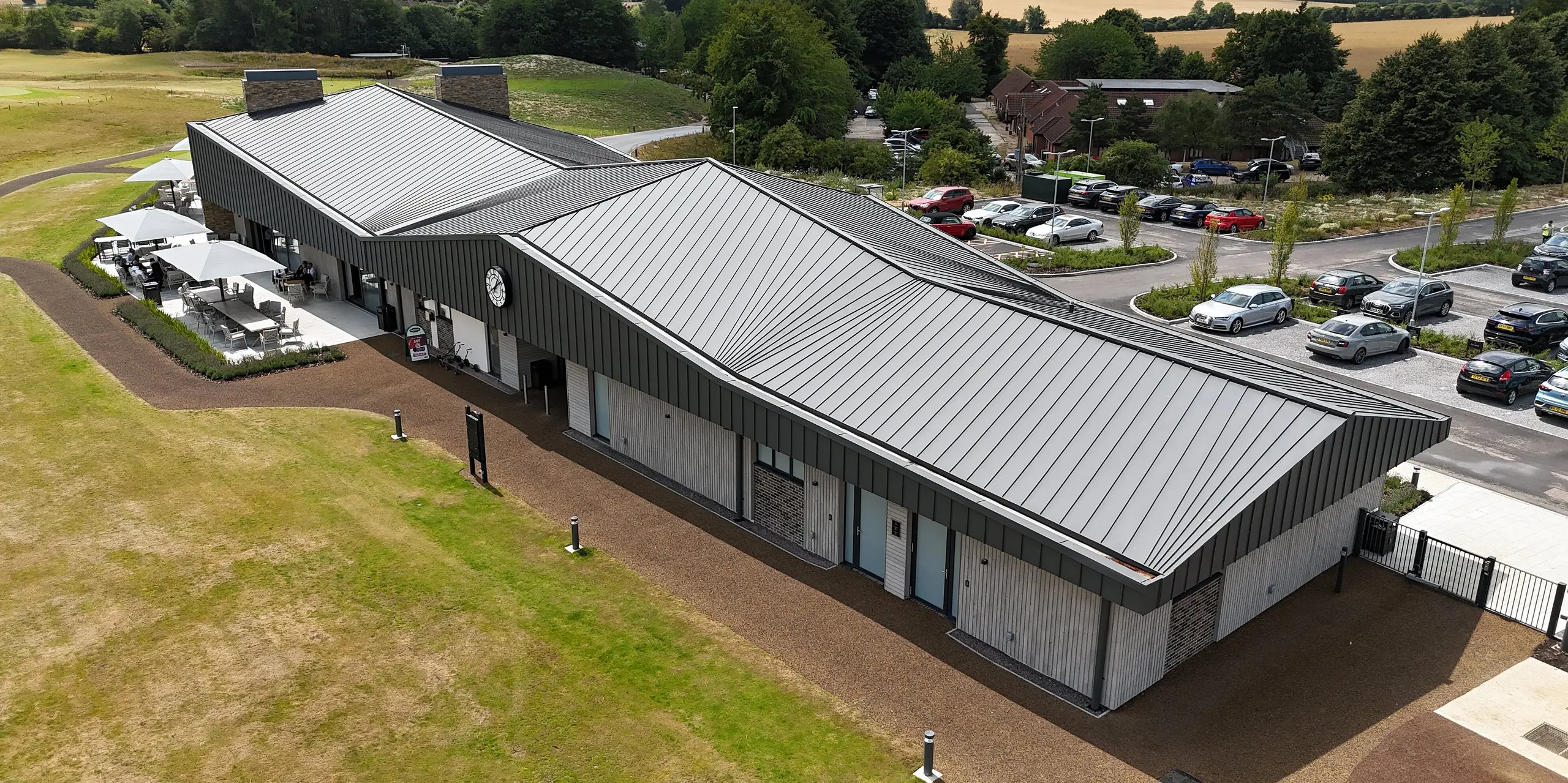 Le Basingstoke Golf Club, dans le Hampshire, arbore un nouveau bâtiment moderne impressionnant, dont la toiture et la partie supérieure de la façade sont habillées d'environ 1 600 m² de joints debout PREFALZ, couleur gris sombre P.10. La pureté des lignes et l'élégance de la toiture créent des accents saisissants et s'harmonisent avec le cadre verdoyant du golf. La partie inférieure de la façade, réalisée en panneaux de bois et en briques, complète ce design raffiné.