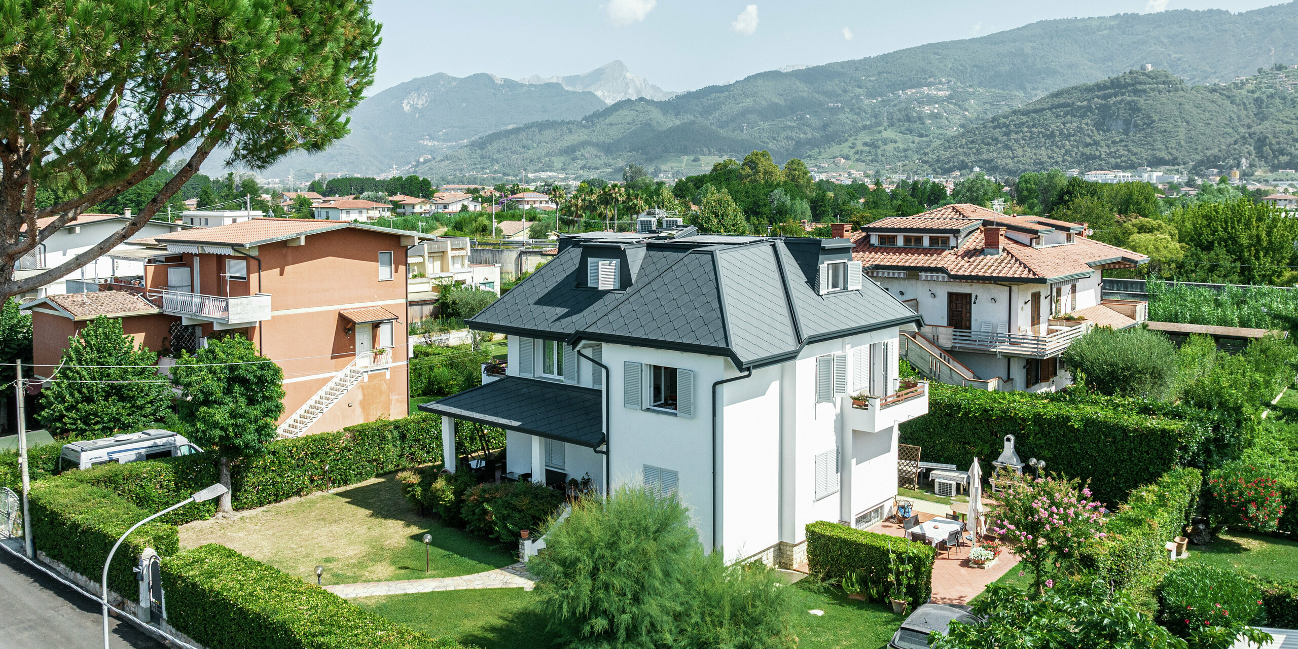 L'élégante maison individuelle de Montignoso, en Italie, impressionne par sa toiture PREFA de haute qualité en aluminium robuste. Le toit en losanges PREFA 44 × 44 en P.10 gris pierre offre une solution moderne, résistante aux intempéries et durable. La toiture en aluminium s'intègre harmonieusement dans l'environnement méditerranéen et offre une protection optimale contre les tempêtes, la corrosion et les rayons UV. La finition précise et le design élégant soulignent la haute qualité des produits PREFA.
