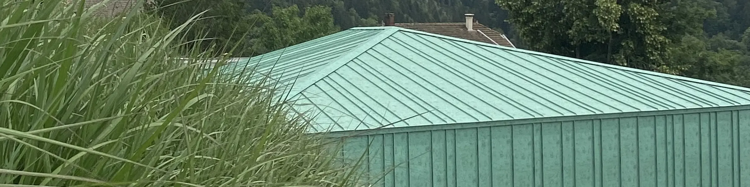 Vue éloignée la nouvelle crèche des Adrets dont la toiture et la façade sont habillées de joint debout Prefalz dans la teinte P.10 vert-de-gris