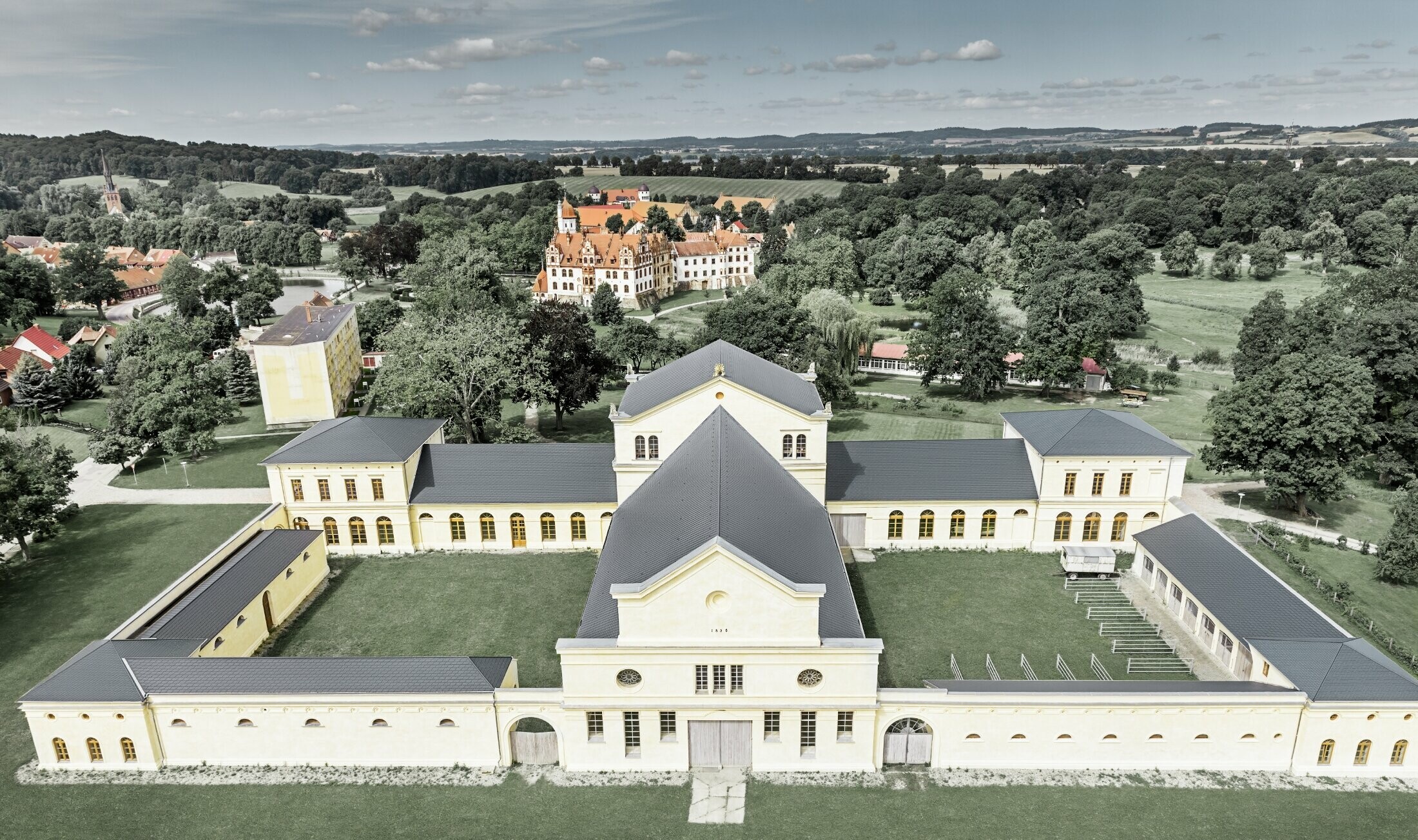 Prise de vue aérienne des écuries de Basedow ; rénové, le château de style renaissance présente lui aussi une nouvelle toiture réalisée avec le bardeau de toiture PREFA couleur anthracite.