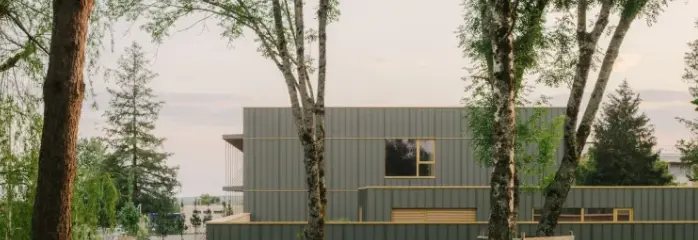 Vue éloignée du collège Maryse Bastié dont la façade a été entièrement rénové avec PREFA. On aperçoit la nature et les arbres en premier plan.