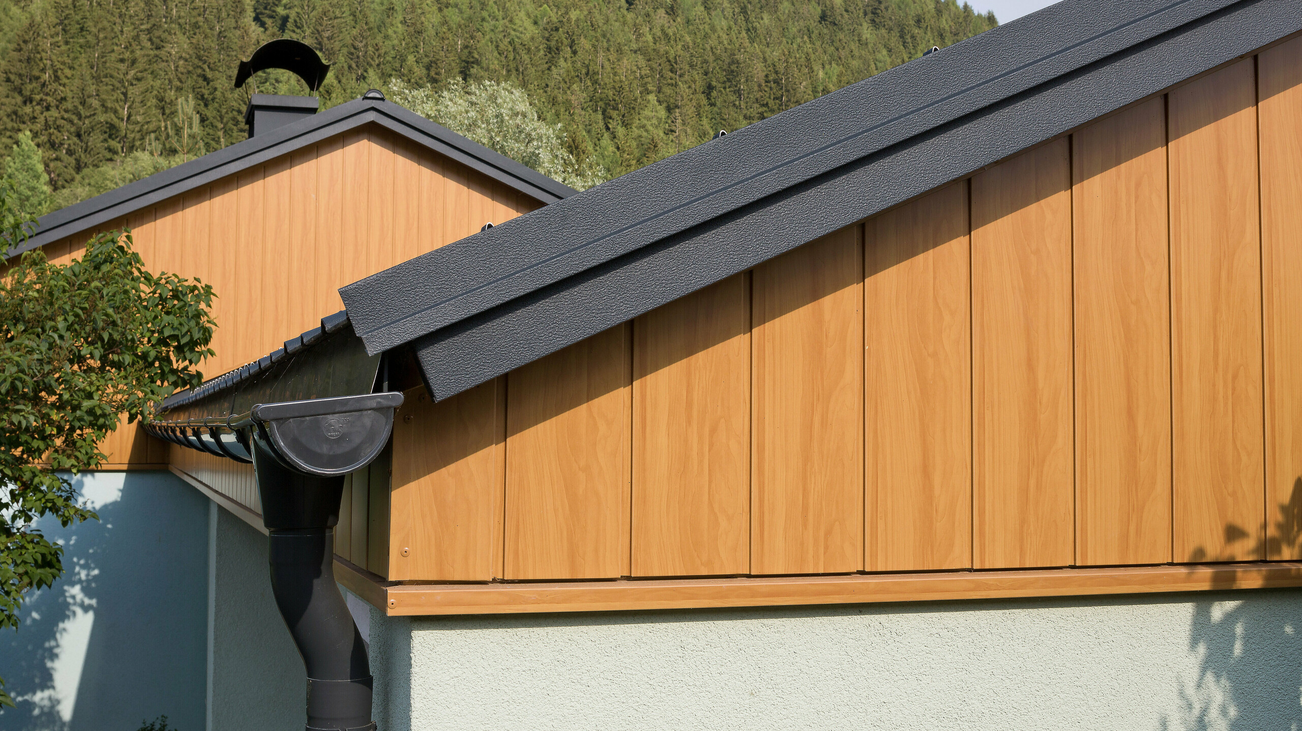 Revêtement de pignon avec les Sidings en aluminium de PREFA couleur chêne naturel montés à la verticale avec une gouttière PREFA anthracite.