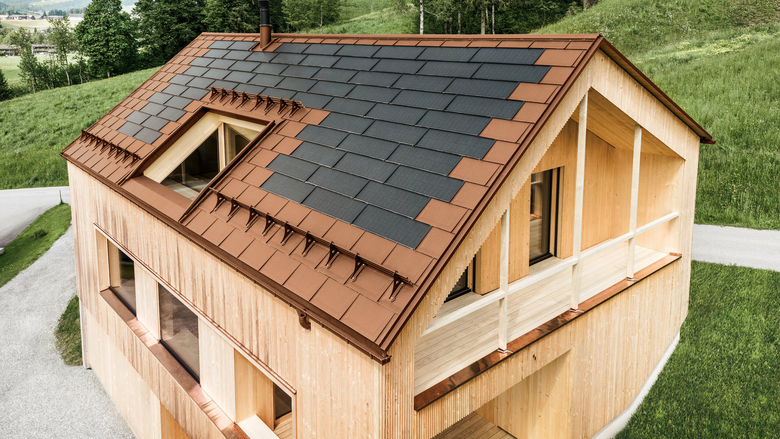 Maison individuelle située dans la localité autrichienne d'Egg, avec le panneau solaire de toiture PREFA et le panneau de toiture R.16 en rouge brique, combinés à une façade en bois.