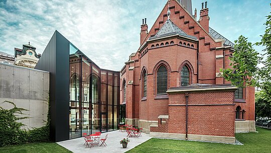 L'image révèle l'impressionnant nouveau bâtiment reliant l'église rouge historique à la bibliothèque scientifique moderne d'Olomouc. La perspective dévoile l'arrière du bâtiment et sa terrasse accueillante. L'élégante façade en panneaux composites d'aluminium noir PREFABOND apporte une touche de modernité saisissante et contraste avec style avec la brique rouge de l'église. La grande précision de la pose et l'utilisation de matériaux durables comme l'aluminium garantissent une harmonieuse alliance entre tradition et innovation. Ces panneaux de pointe sont non seulement esthétiques, mais aussi très fonctionnels et résistants, faisant de ce projet un chef-d'œuvre d'architecture moderne.