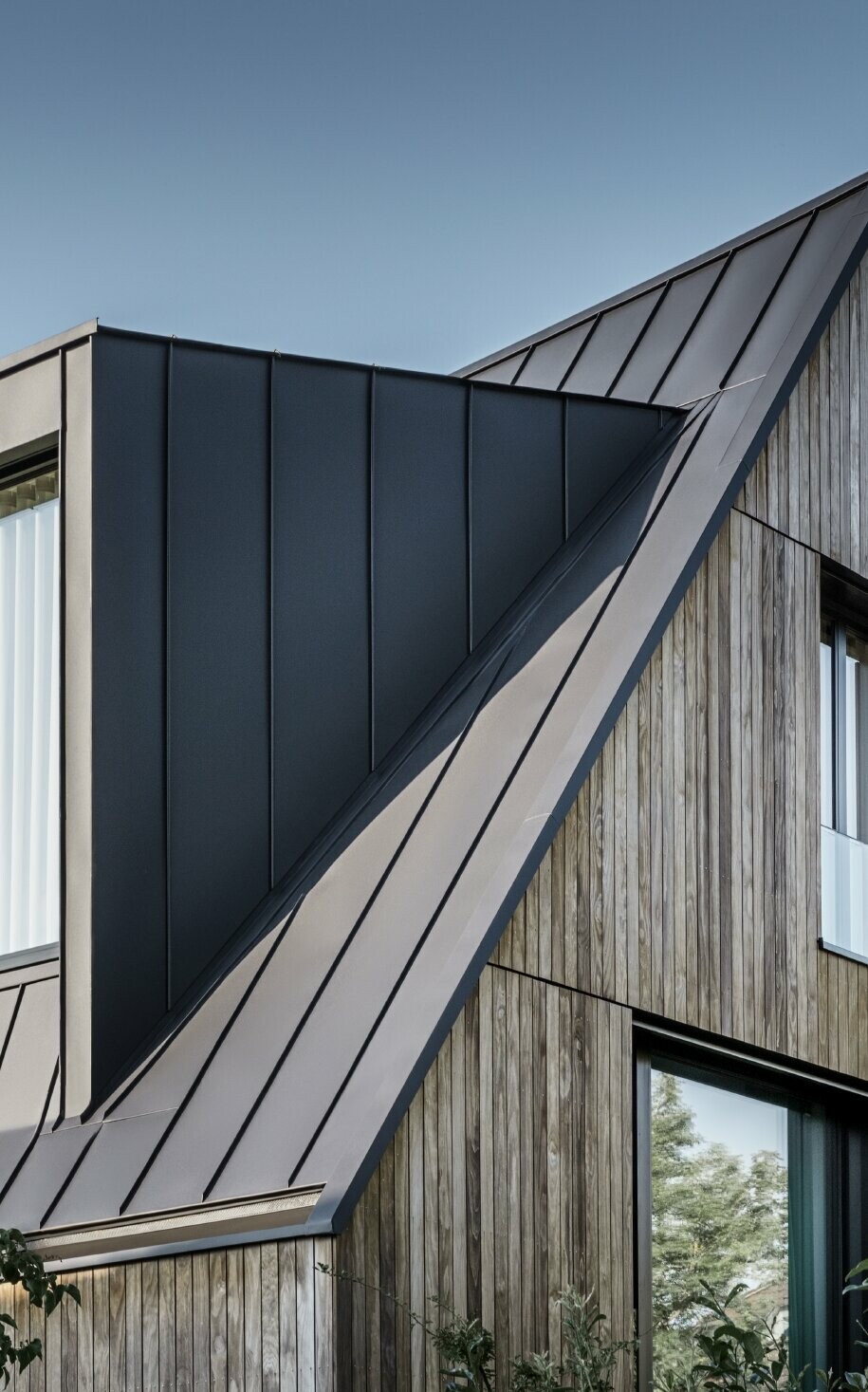 Toit à pignon raide avec grande lucarne, recouvert avec PREFALZ de PREFA en anthracite et joints debout du toit combinés avec la façade en bois