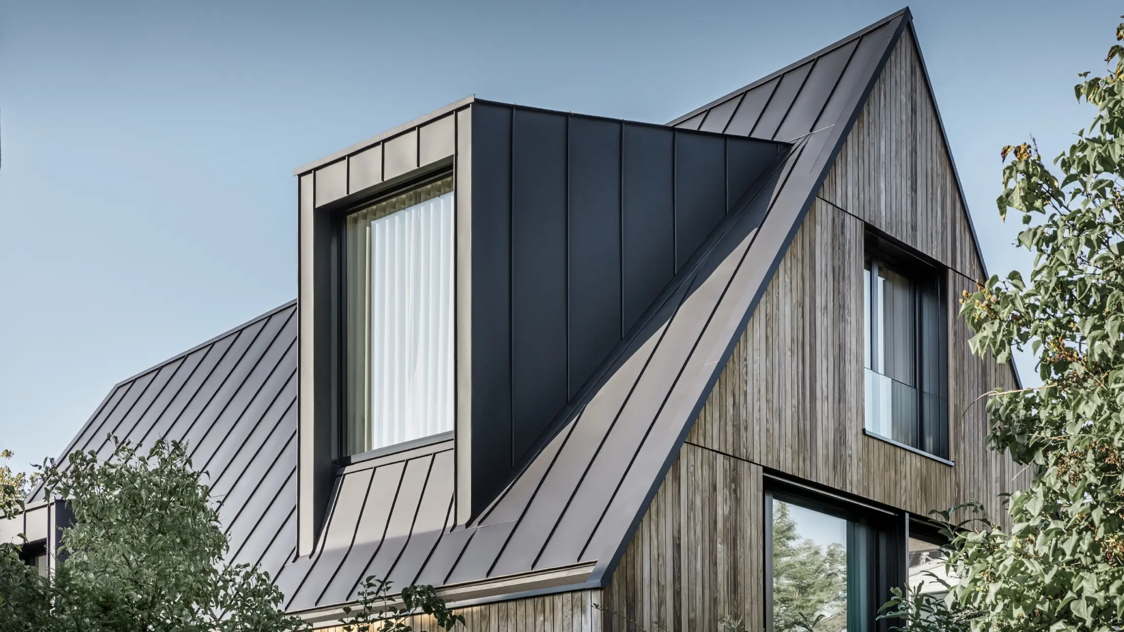 Toit à pignon raide avec grande lucarne, recouvert avec PREFALZ de PREFA en anthracite et joints debout du toit combinés avec la façade en bois