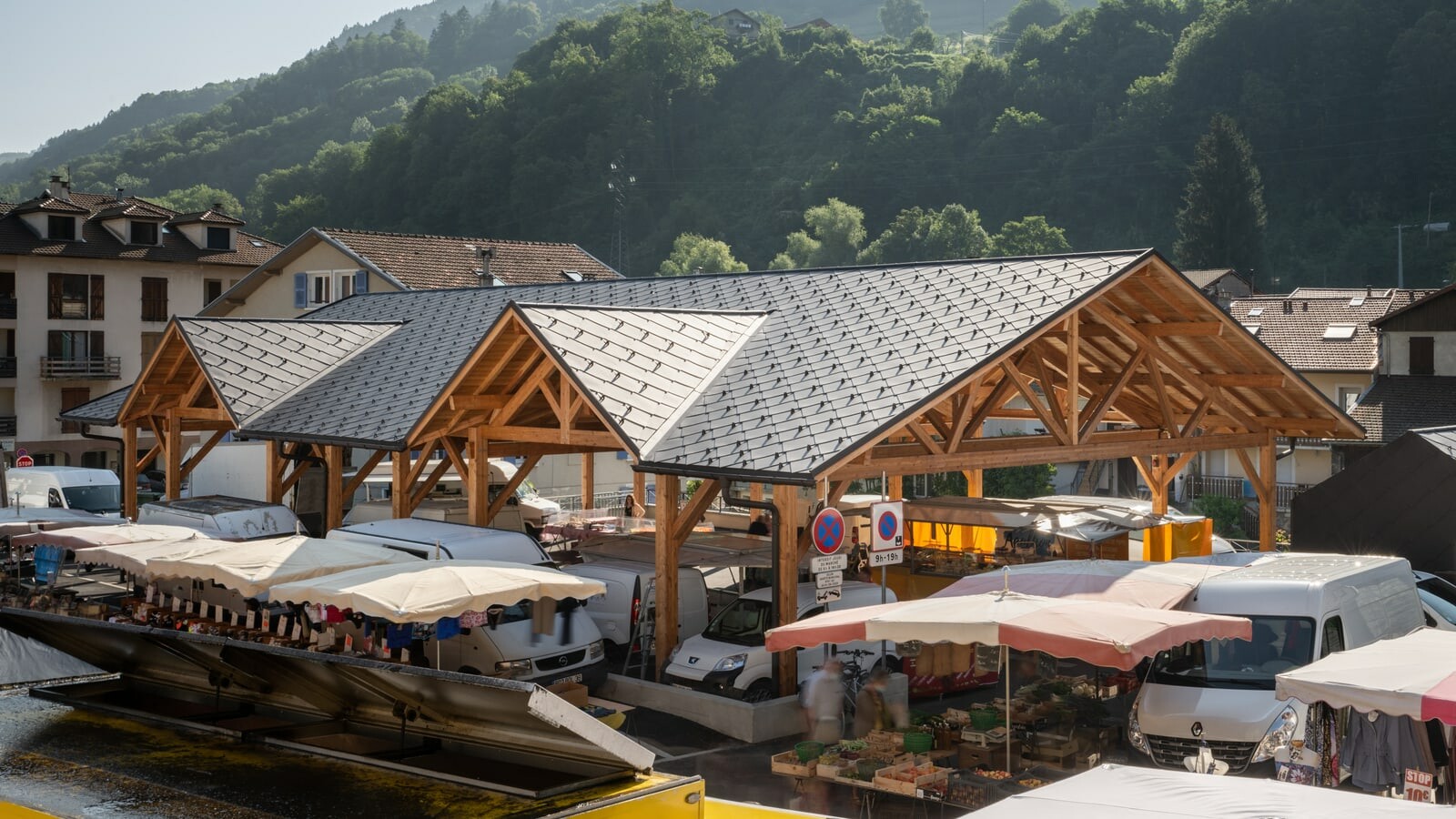 Vue de haut de la halle couverte d'Allevard un jour de marché. La couverture neuve a été choisie en losange de toiture 44x44 PREFA, dans la teinte P.10 brun noisette.