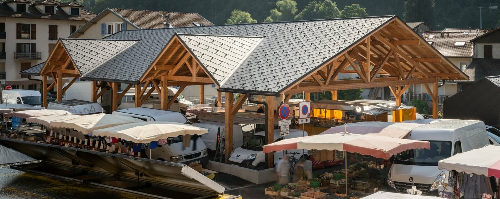 Vue de haut de la halle couverte d'Allevard un jour de marché. La couverture neuve a été choisie en losange de toiture 44x44 PREFA, dans la teinte P.10 brun noisette.