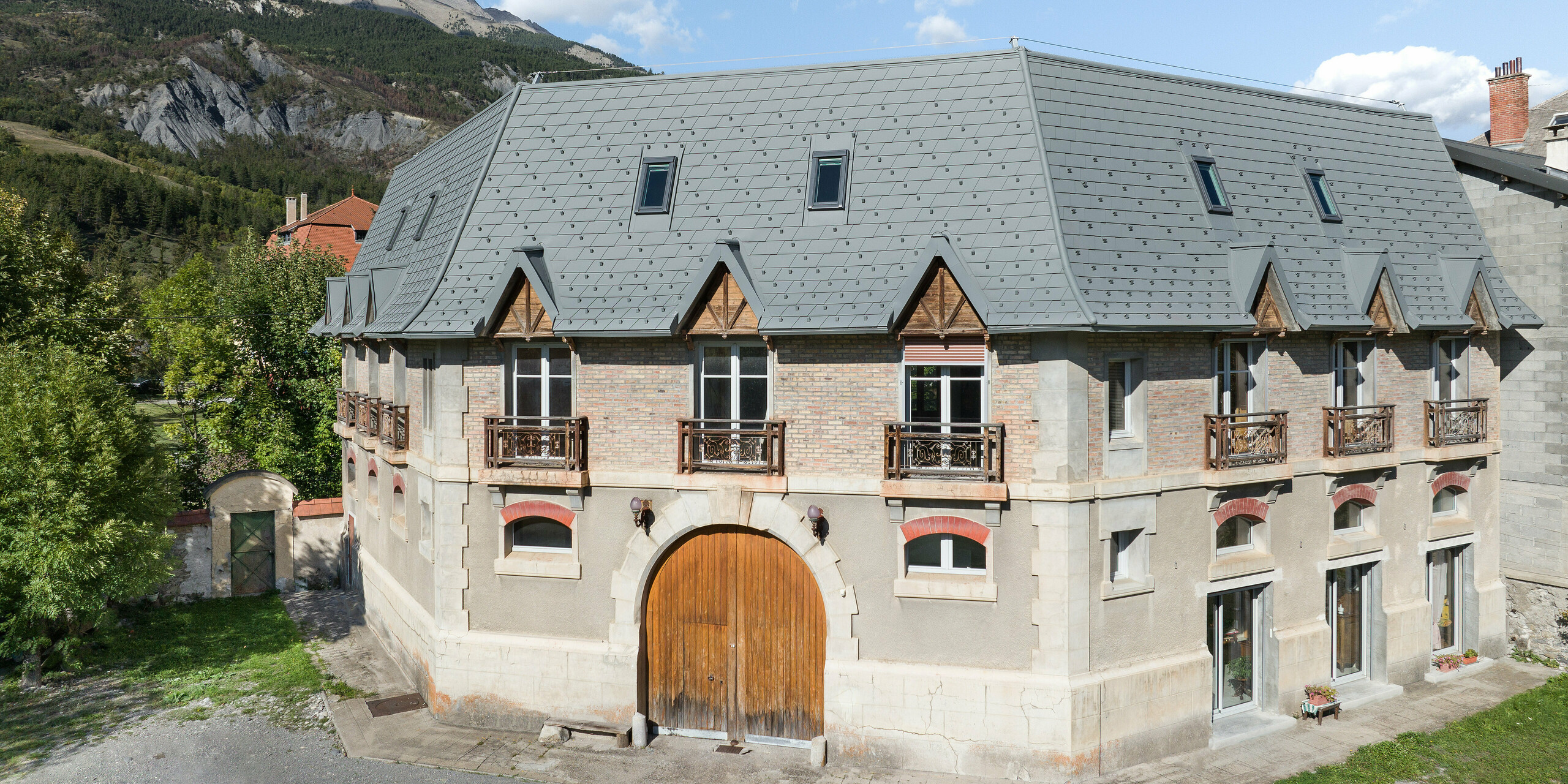 Vue de face d'une propriété à Barcelonnette, France. Le vaste toit a été rénové avec le bardeau de toiture PREFA en P.10 gris souris.
