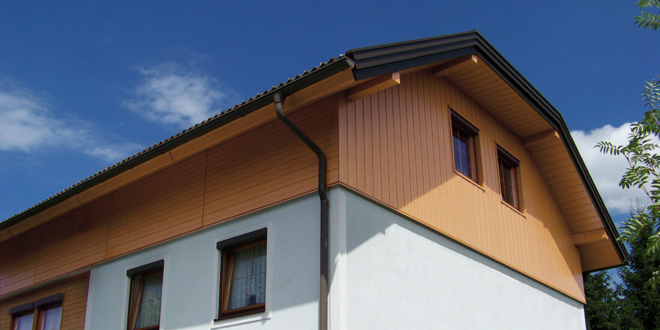 Grande maison individuelle à toit à demi-croupe et revêtement des pignons avec des Sidings PREFA imitation bois clair