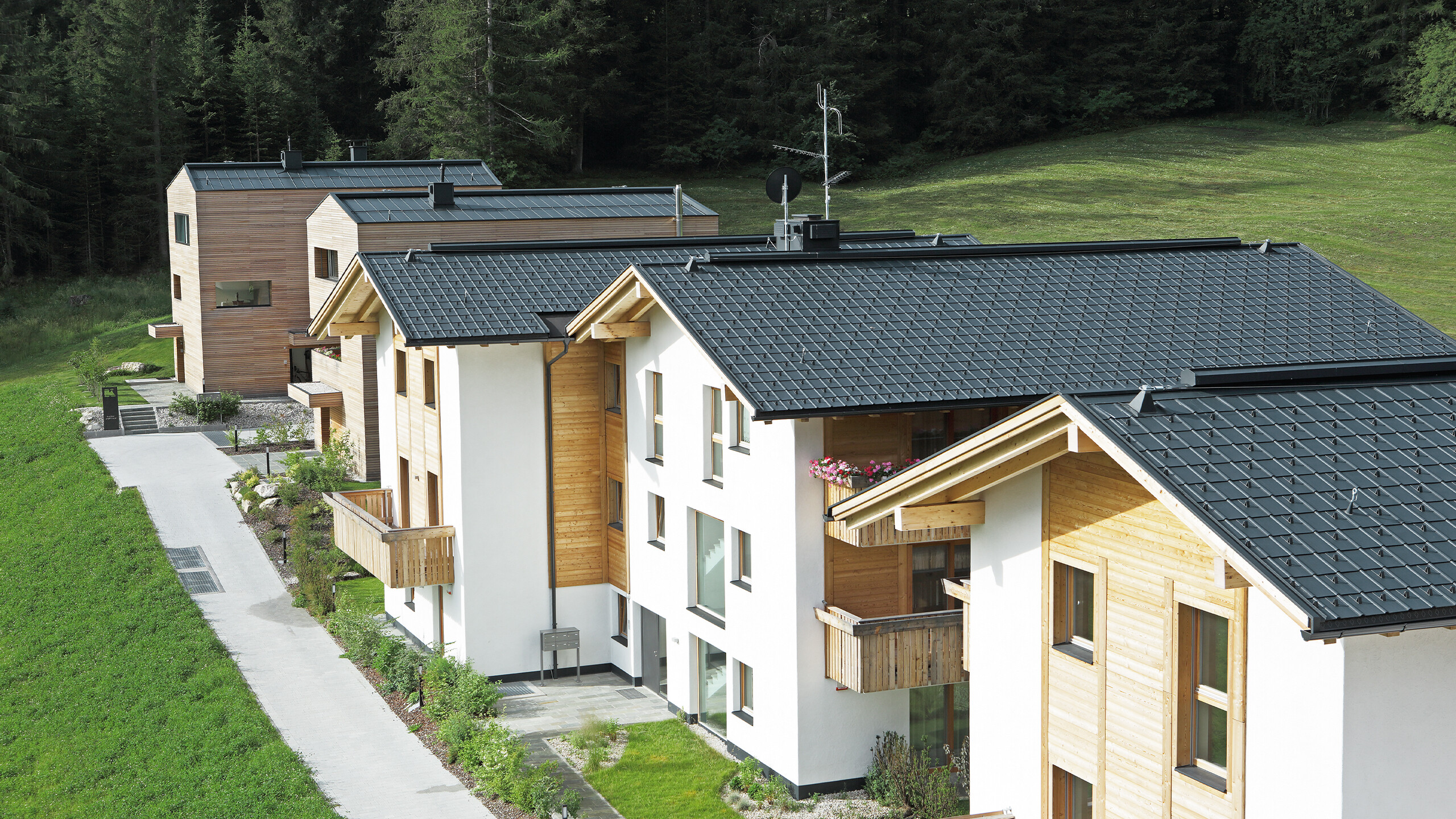 Vue des cinq immeubles d'habitation à Corvara, recouverts de tuiles PREFA et d'un joint debout en aluminium anthracite résistant aux tempêtes.