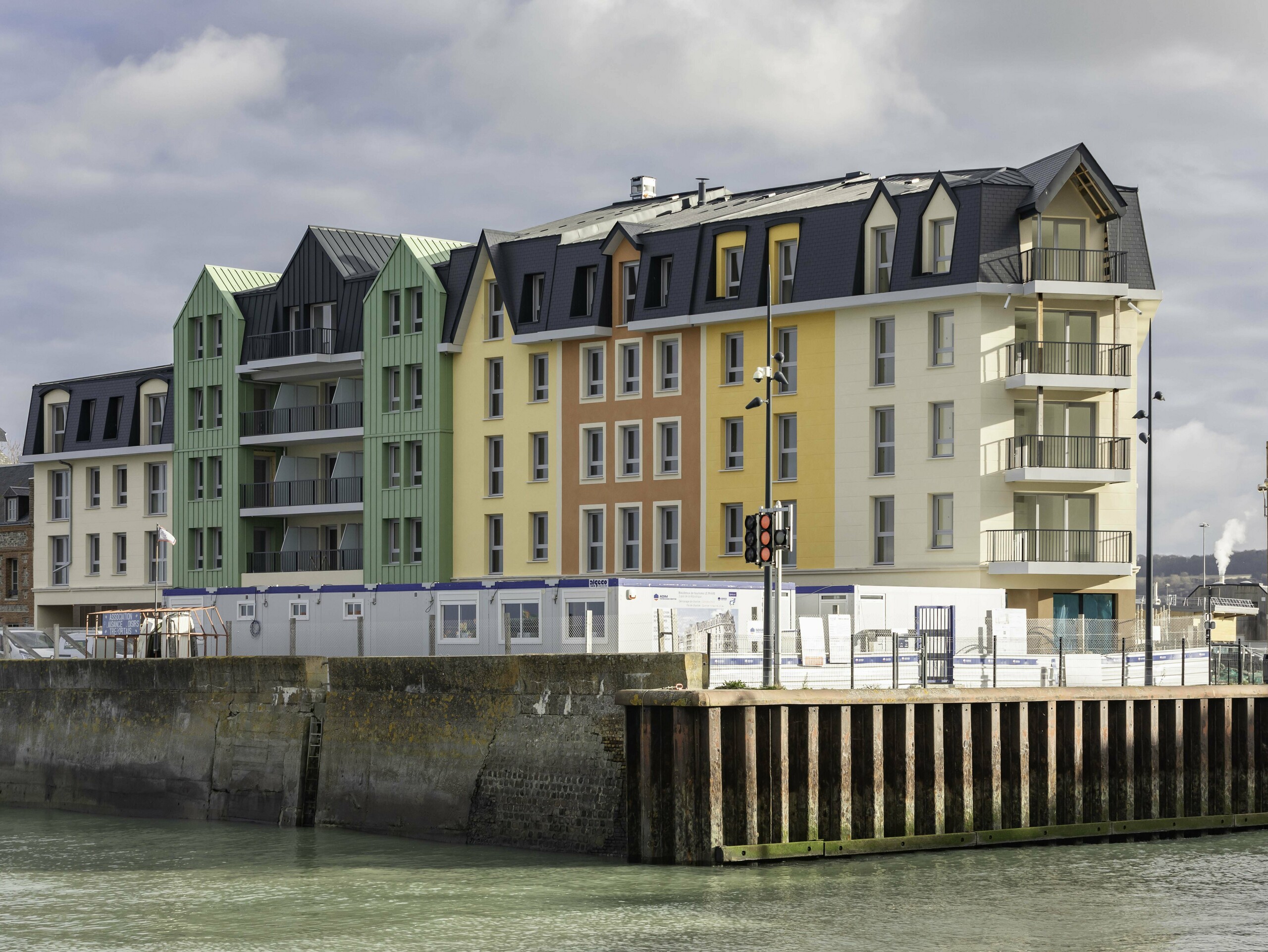 Vue éloignée de la résidence Le Phare à Le Tréport. Ses façades rénovée arbore une combinaison entre des crépis jaunes orangées et des façade en aluminium PREFA vert olive et anthracite.