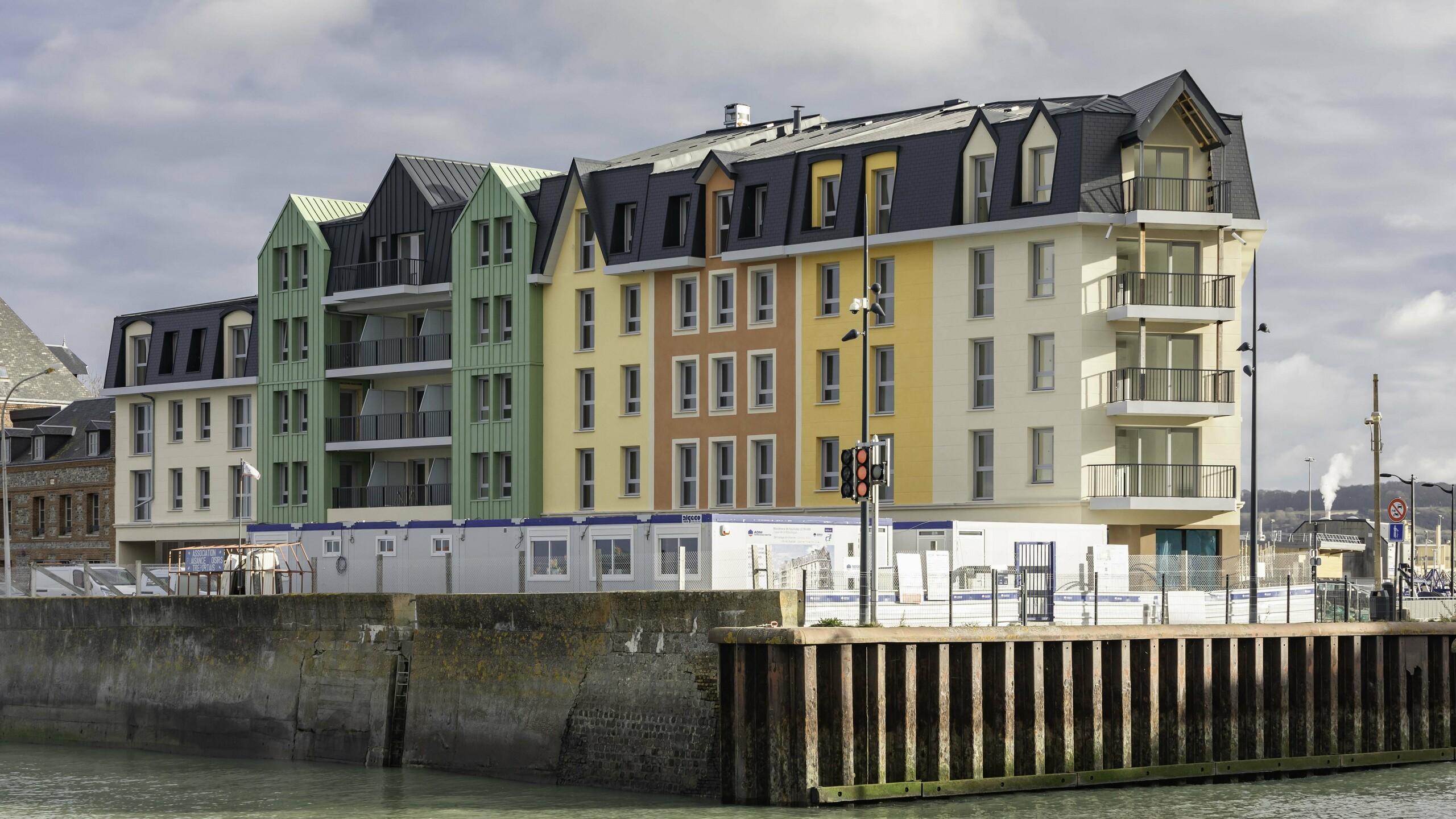 Vue éloignée de la résidence Le Phare à Le Tréport. Ses façades rénovée arbore une combinaison entre des crépis jaunes orangées et des façade en aluminium PREFA vert olive et anthracite.