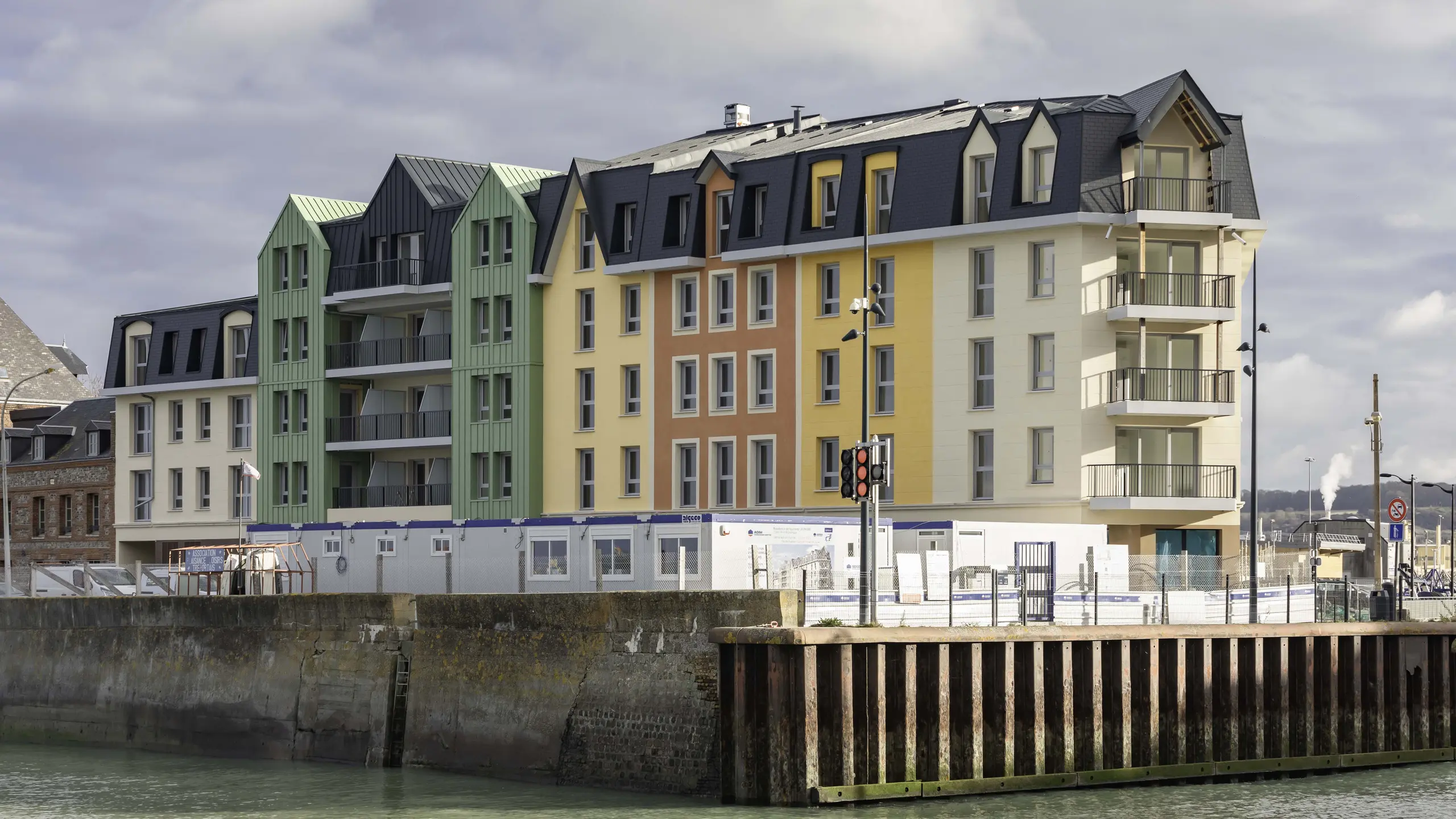 Vue éloignée de la résidence Le Phare à Le Tréport. Ses façades rénovée arbore une combinaison entre des crépis jaunes orangées et des façade en aluminium PREFA vert olive et anthracite.