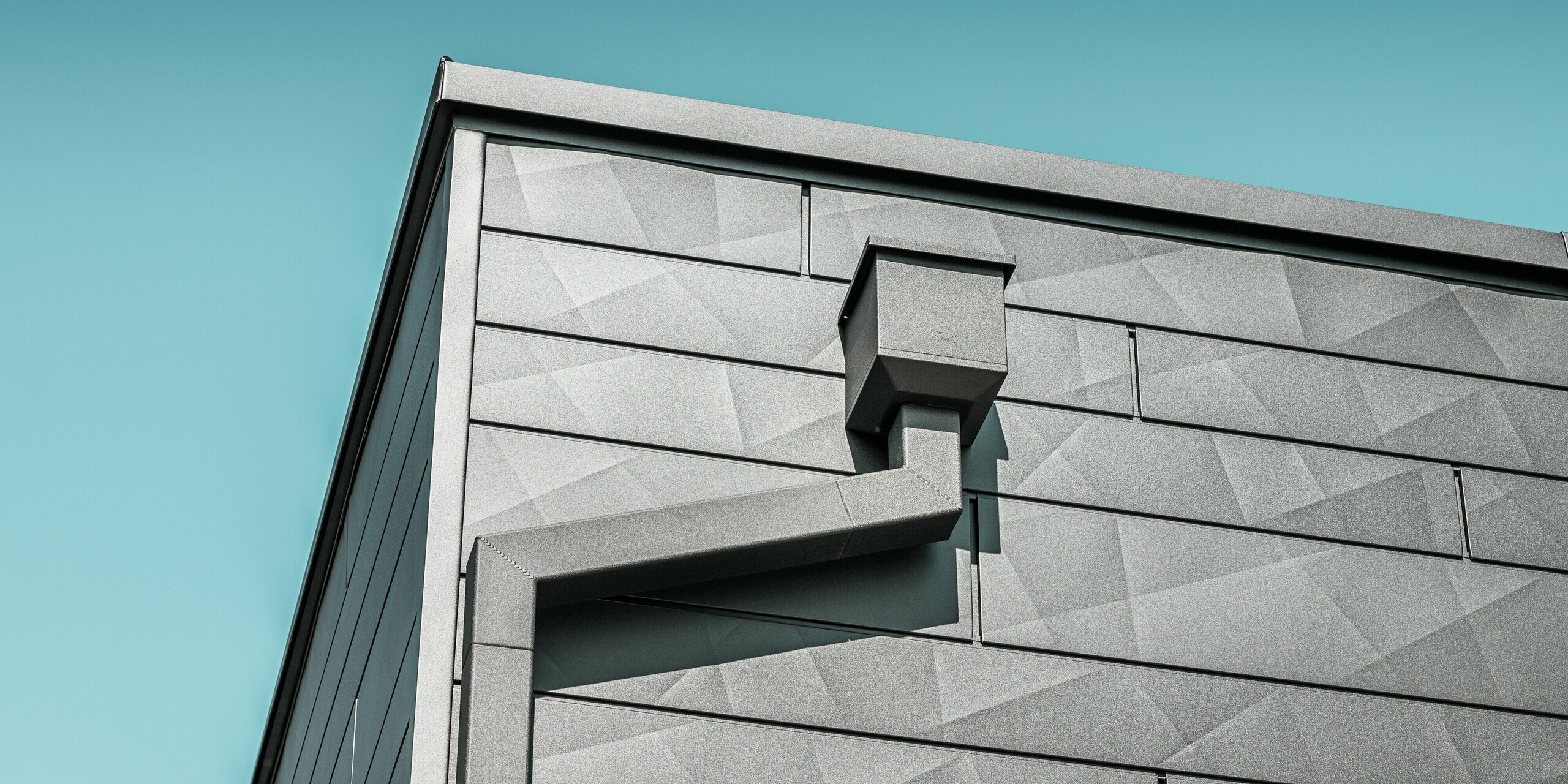 La façade de la maison individuelle rénovée de Teuschnitz est ornée de panneaux en aluminium Siding.X PREFA couleur P.10 noir, à la texture géométrique unique. Le collecteur d'eau et le tuyau carré PREFA s'intègrent élégamment au design et offrent une solution d'évacuation fonctionnelle. La finition soignée et l'intégration harmonieuse des éléments soulignent l'esthétique et la durabilité des produits en aluminium PREFA.
