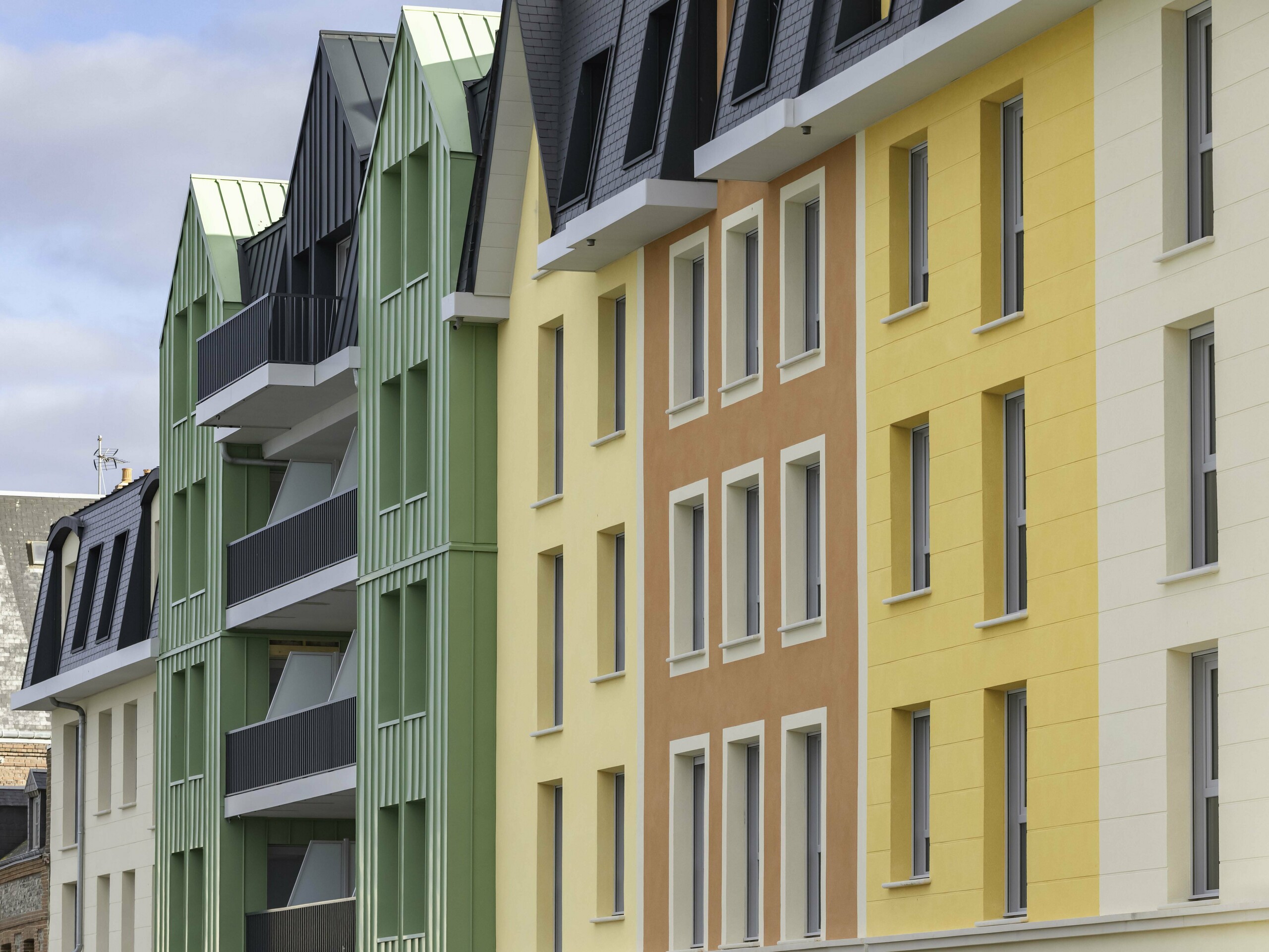 Zoom sur les façades colorées de la résidence Le Phare à Le Tréport. Une combinaison entre des crépis jaunes orangées et des façade en aluminium PREFA vert olive et anthracite.