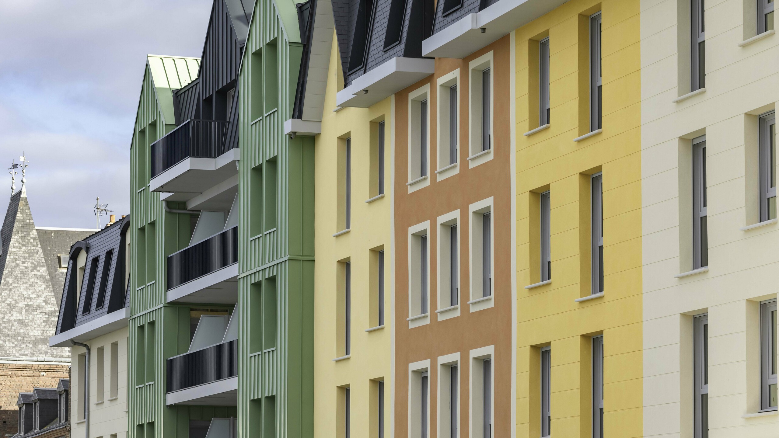 Zoom sur les façades colorées de la résidence Le Phare à Le Tréport. Une combinaison entre des crépis jaunes orangées et des façade en aluminium PREFA vert olive et anthracite.