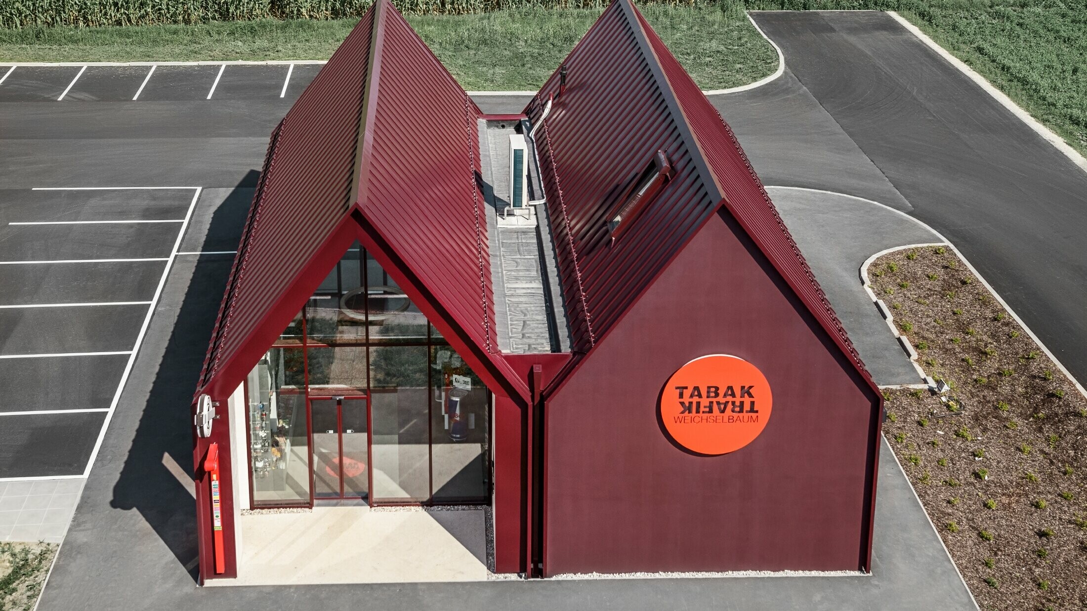 Bureau de tabac moderne au toit à deux versants sans saillie de façade — Enveloppe en aluminium PREFA à joints debout et joints angulaires rouge-noir (couleur spéciale)