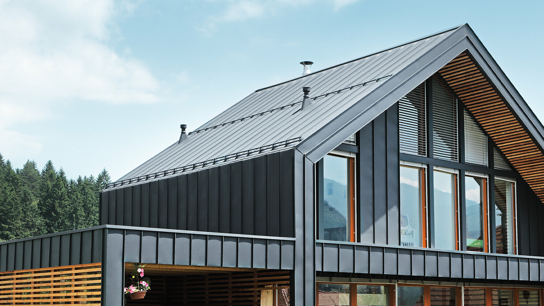 La maison individuelle moderne aux grandes surfaces vitrées a été revêtue de l’élément Prefalz de PREFA. Le toit à joint debout et la façade à joint angulaire debout constituent un bel habillage de bâtiment anthracite.