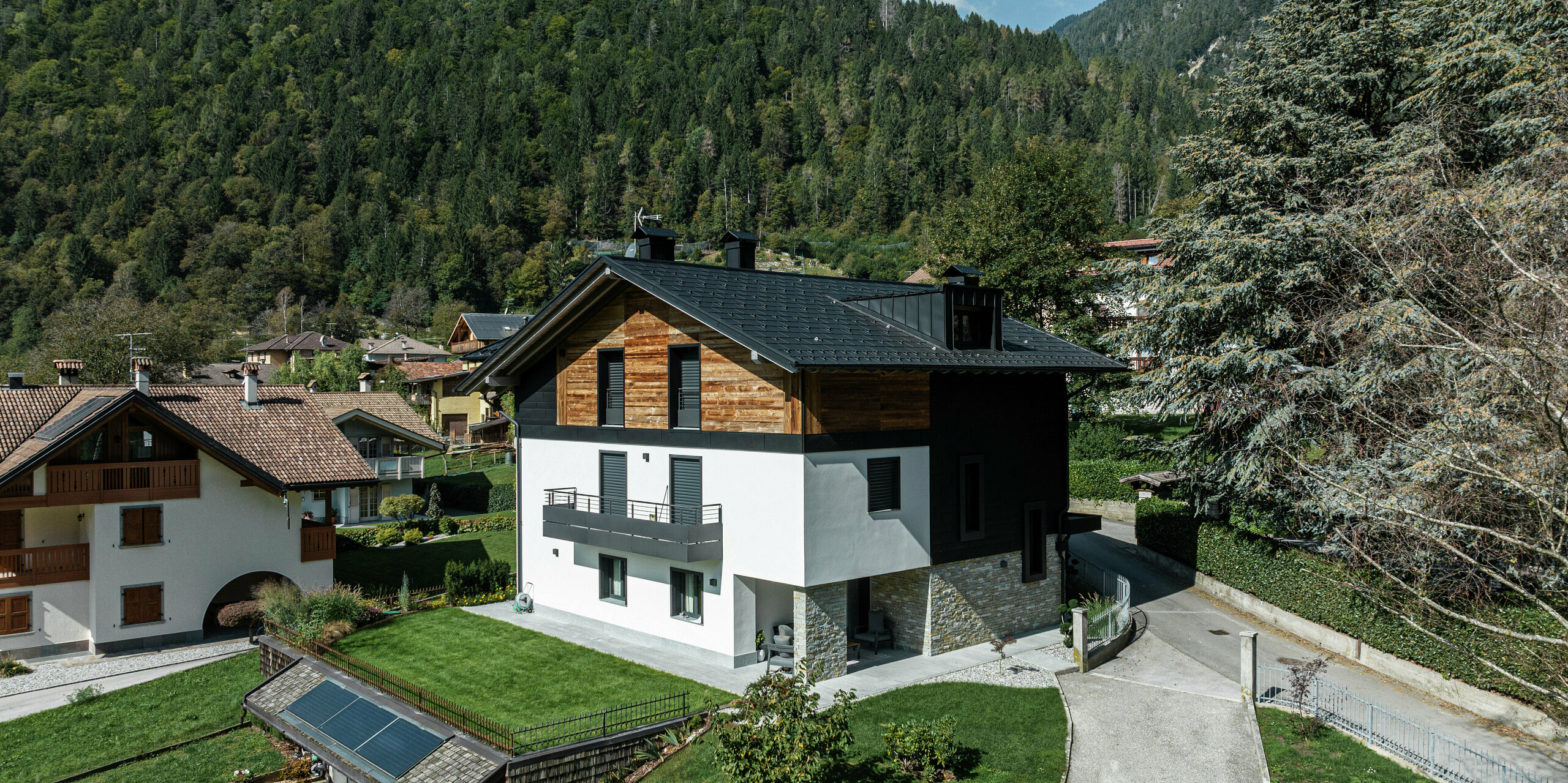 Bâtiment résidentiel moderne à Pelugo, en Italie, après rénovation et réhabilitation écoénergétique. Le toit a été recouvert du R.16 PREFA durable en P.10 anthracite, et la façade a reçu un aspect moderne et durable avec PREFA Siding.X en P.10 anthracite. La combinaison de l'aluminium, du bois et du plâtre crée une architecture harmonieuse et résistante aux intempéries.