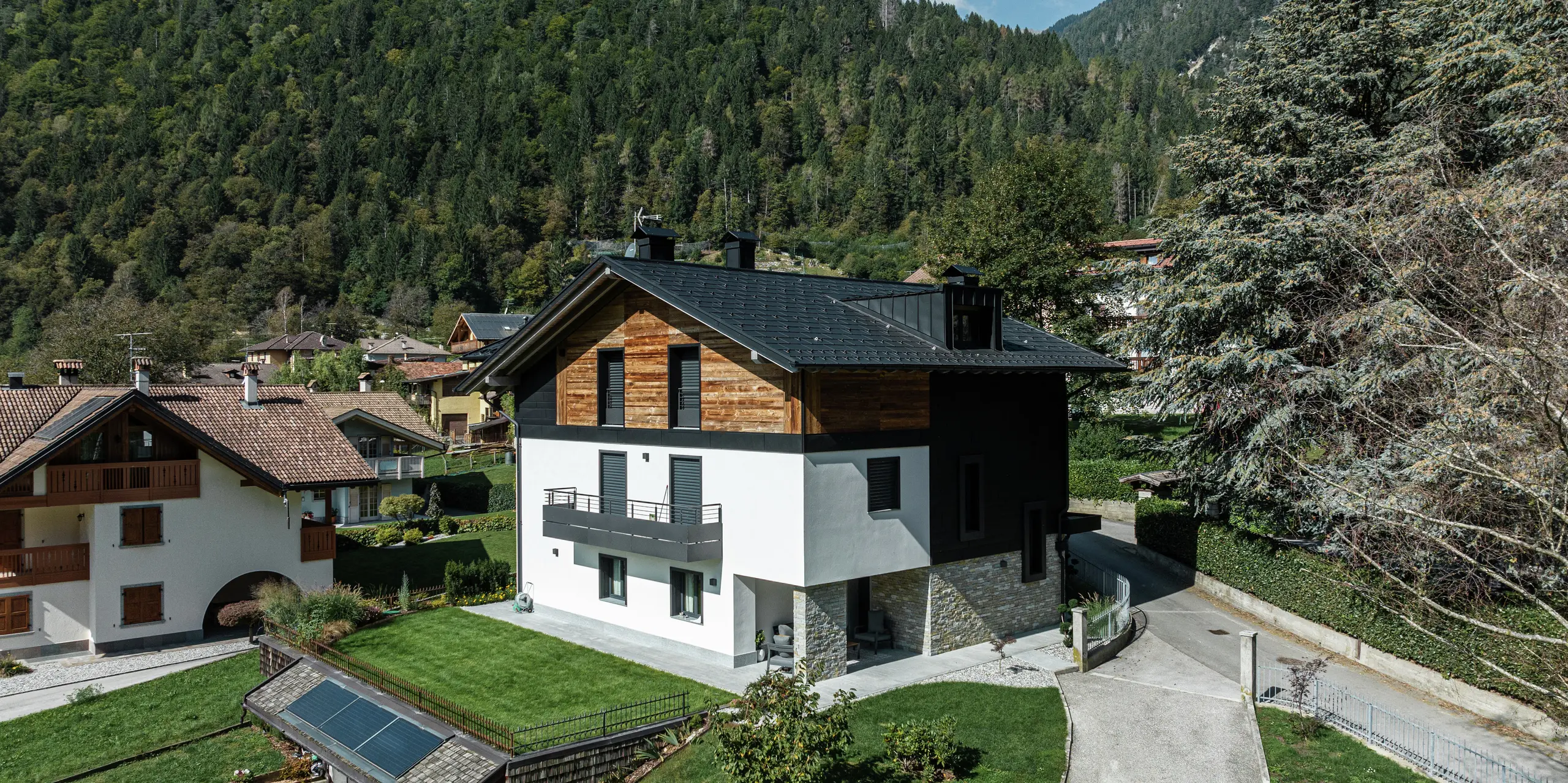 Bâtiment résidentiel moderne à Pelugo, en Italie, après rénovation et réhabilitation écoénergétique. Le toit a été recouvert du R.16 PREFA durable en P.10 anthracite, et la façade a reçu un aspect moderne et durable avec PREFA Siding.X en P.10 anthracite. La combinaison de l'aluminium, du bois et du plâtre crée une architecture harmonieuse et résistante aux intempéries.