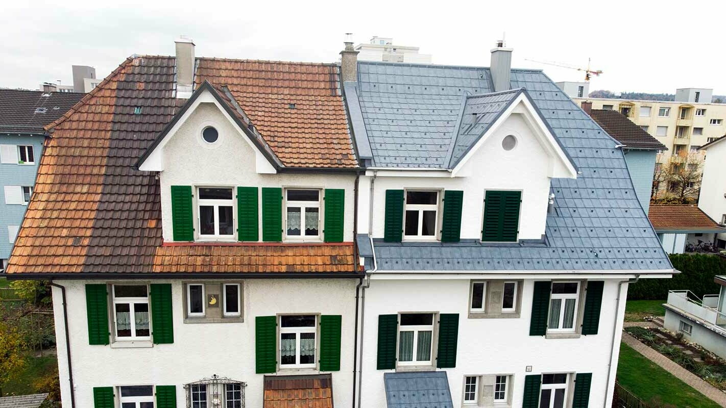 Moitié de maison jumelée en Suisse. La partie gauche du bâtiment n’a pas encore été rénovée et est encore recouverte de tuiles sales. La partie droite du bâtiment a été recouverte à l’aide de tuiles PREFA couleur gris pierre.