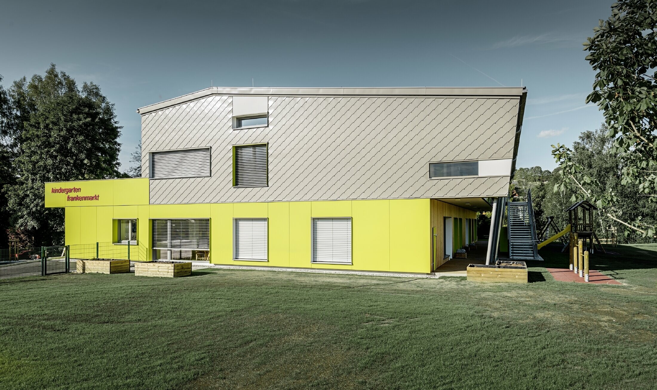 Le jardin d’enfants a été partiellement habillé avec le losange de façade 29 PREFA couleur bronze. Cette partie du bâtiment ne présente pas d’avancée de toit. Le reste de la façade a été habillé de panneaux de façade couleur jaune.