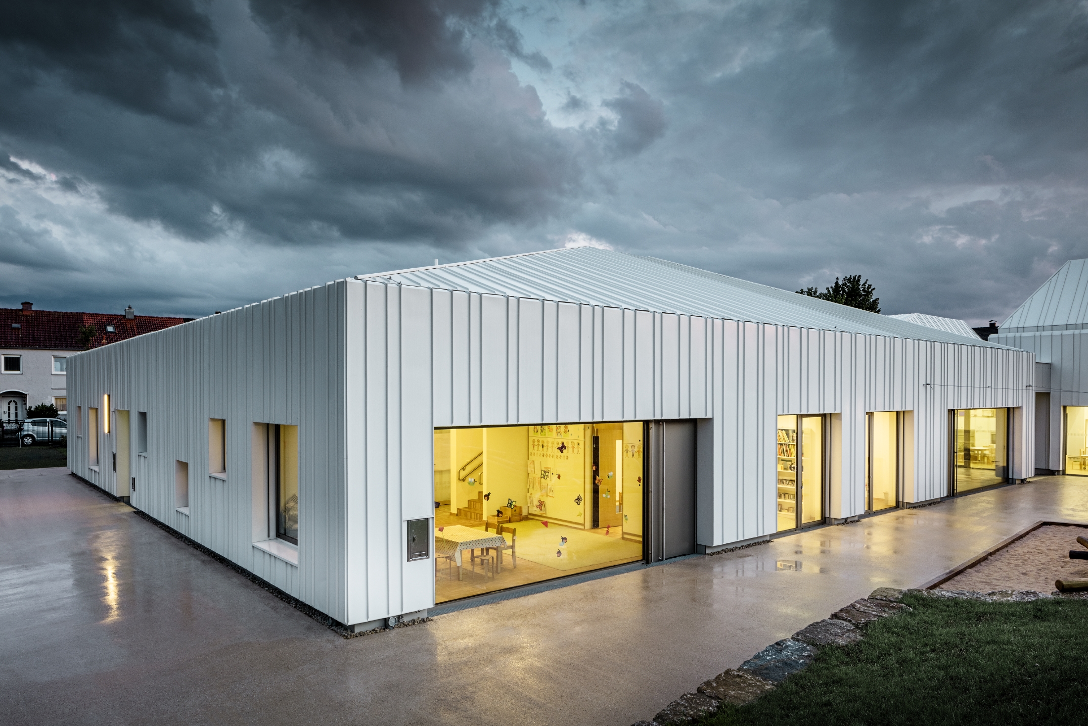 Crèche à Niederwerrn avec toit et façade PREFALZ dans la couleur blanc pur, avec différentes largeurs de bac, photographiée au crépuscule dans des conditions nuageuses