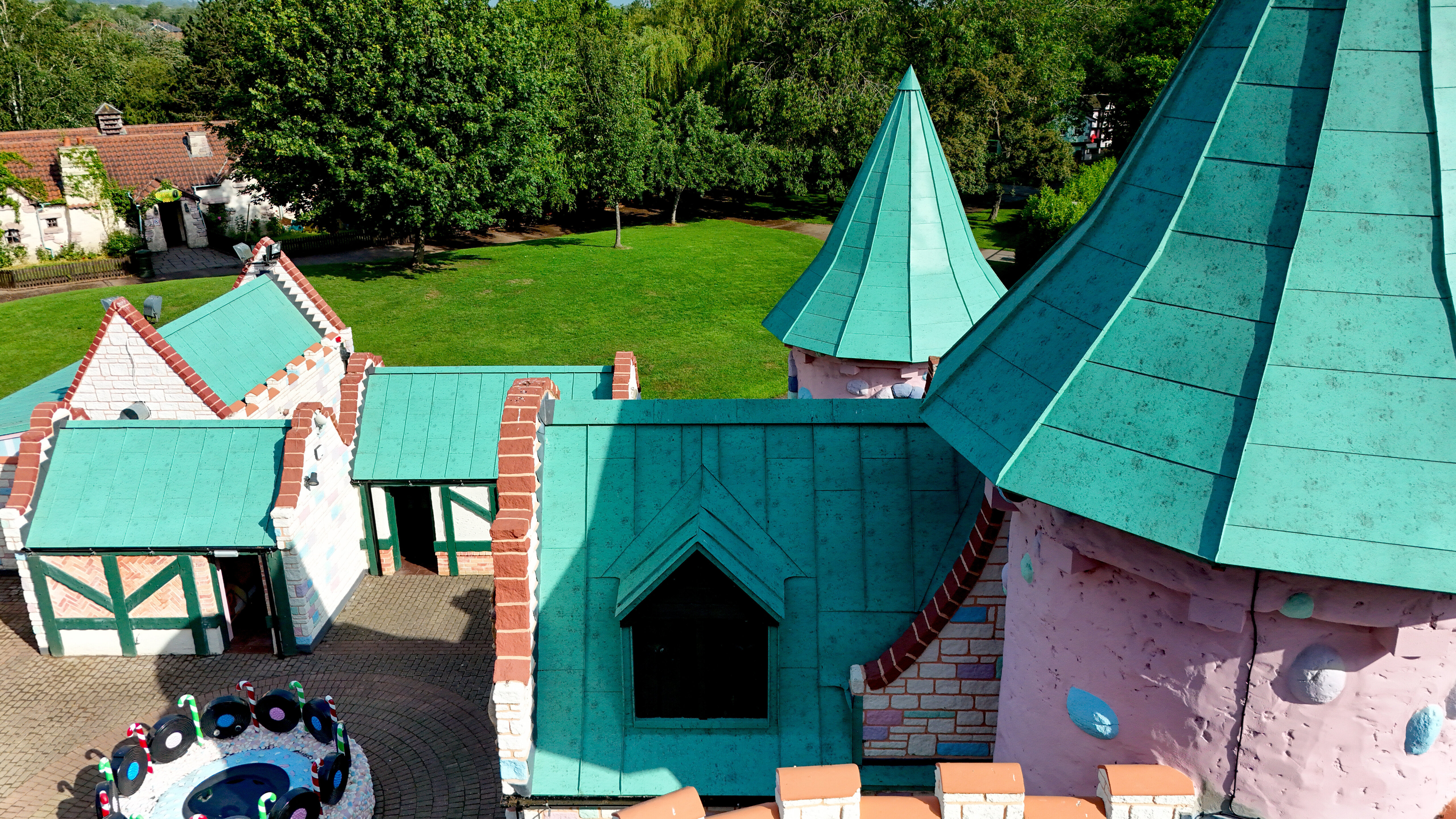 Une perspective détaillée de l'architecture imaginative du château de Sundown Adventureland, mettant en valeur des tours ludiques, des pignons remarquables et des toitures complexes. Les toitures en aluminium PREFALZ, couleur P.10 vert de gris, attirent immédiatement le regard et soulignent les formes uniques grâce à des joints debout impeccables. Même les géométries les plus complexes sont exécutées avec précision. Les toitures PREFALZ offrent par ailleurs une durabilité maximale, une résistance à la corrosion et une protection fiable, idéales pour une architecture de haute qualité et résistante aux intempéries.